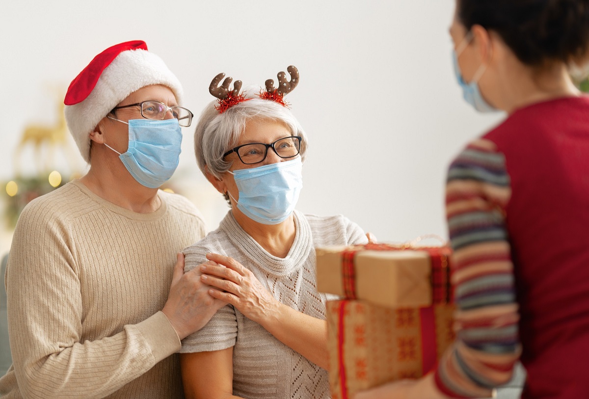 Senior couple with masks wearing holiday hats receive packages from a woman in a mask