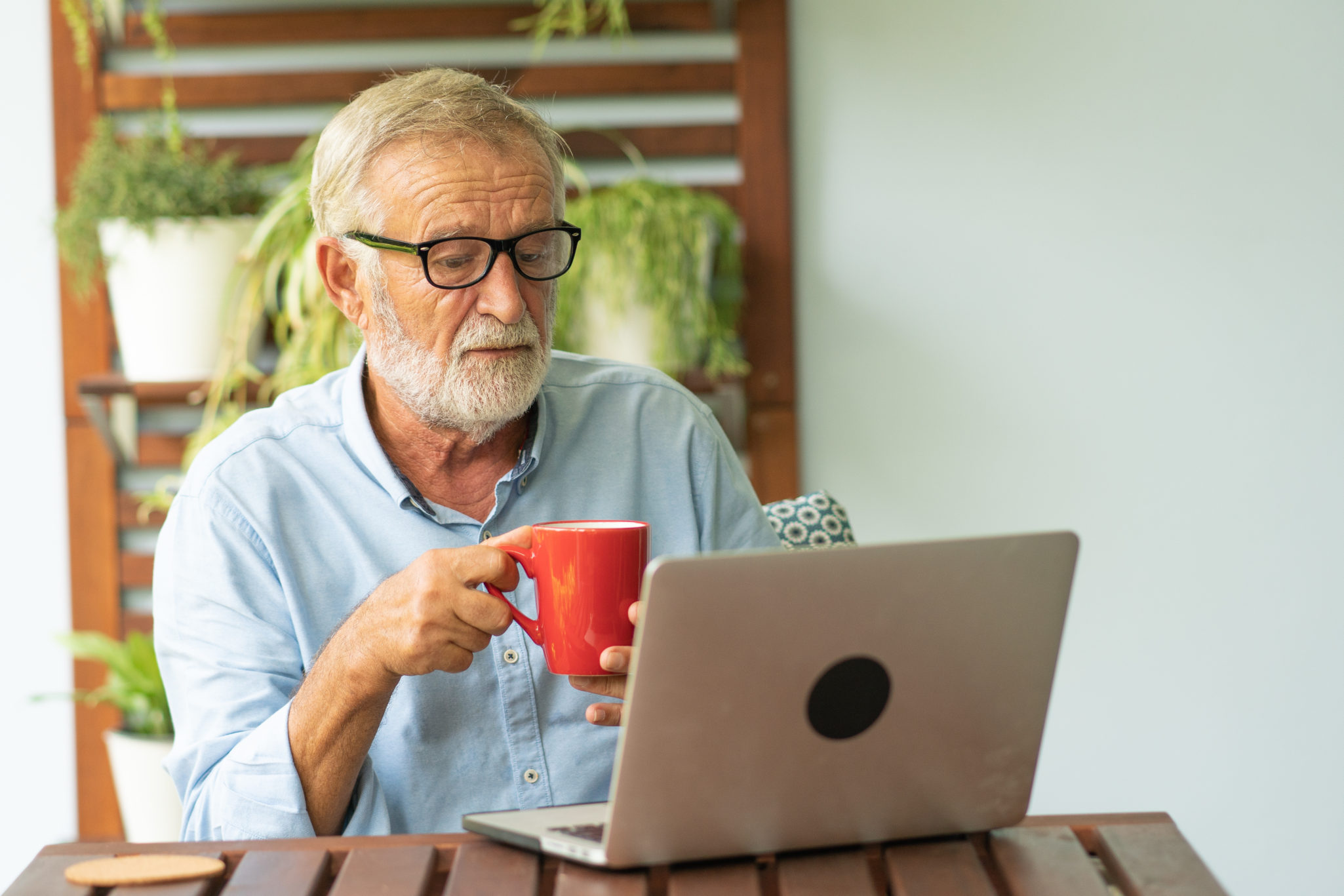 senior man drinking coffee while using his laptop