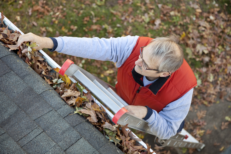Senior man cleans his gutters at home, a maintenance worry that seniors don't need to do in an independent living community.