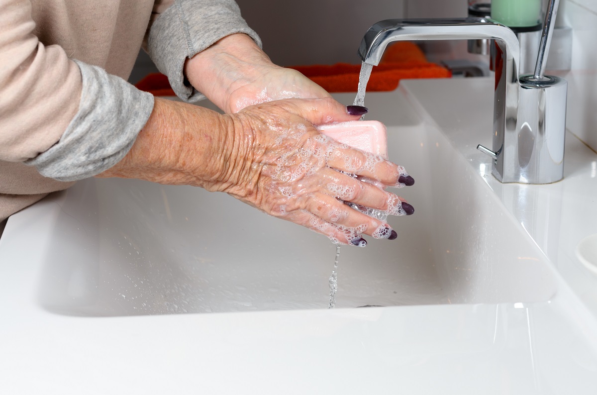 elderly woman washing her hands in the sink with soap and water