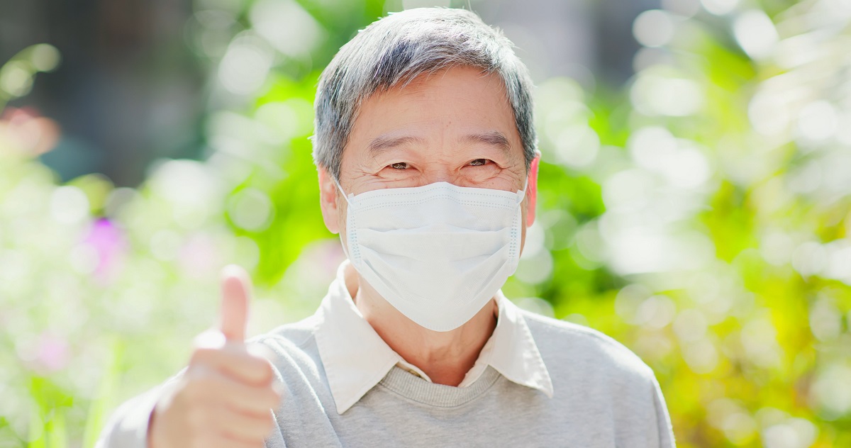 elderly man gives a thumbsup while wearing a mask