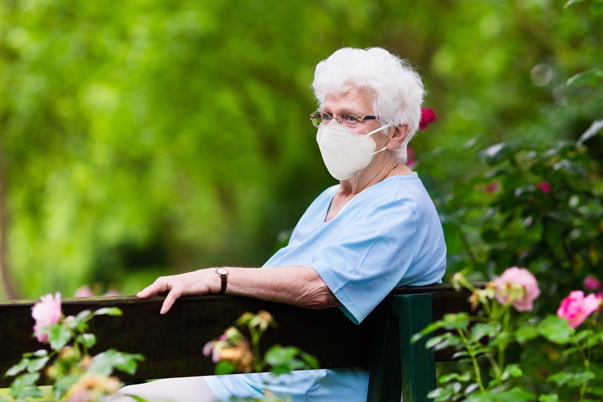 Senior woman in face mask sitting outside in the garden area.