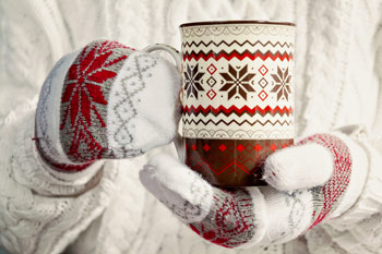 close up shot of a holiday themed mug that someone is holding with mittens